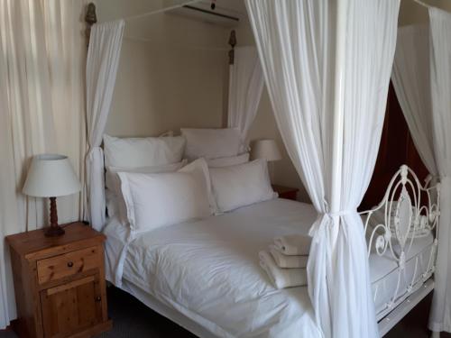 a white bed with white curtains and a wooden night stand at De Kothuize 10 in Graaff-Reinet