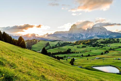 a green hillside with a lake and mountains at Hotel Villa Kastelruth in Castelrotto