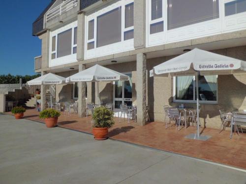 a patio with white umbrellas and tables and chairs at Hotel Brisa in A Lanzada