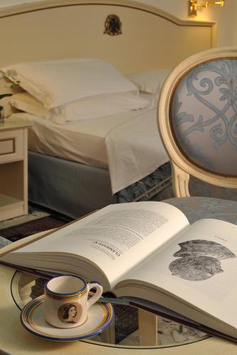 an open book on a table with a cup and a bed at Albergo Hotel Raffaello in Urbino