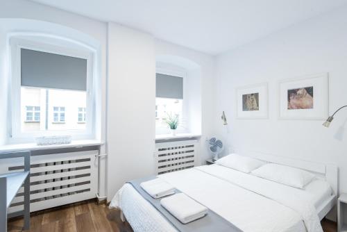 een witte slaapkamer met een bed, een bureau en 2 ramen bij Klimt Apartment in Wrocław