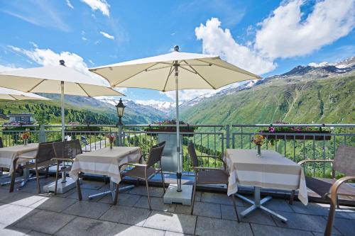 a patio with tables and umbrellas with mountains in the background at Alpenhotel Laurin in Hochgurgl