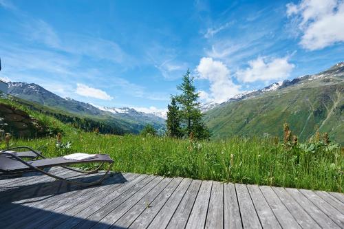 a bench sitting on a wooden deck with mountains in the background at Alpenhotel Laurin in Hochgurgl