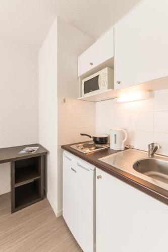 une cuisine avec des armoires blanches et un évier dans l'établissement City Résidence Nantes La Chantrerie, à Nantes
