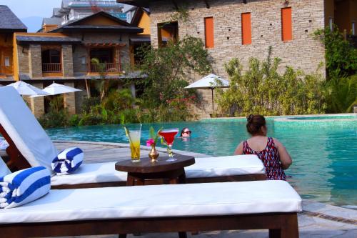 a woman sitting at a table next to a swimming pool at Temple Tree Resort & Spa, Pokhara in Pokhara
