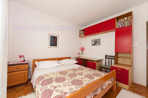 a bedroom with a bed and a desk and red cabinets at Apartman Sulić in Podgora