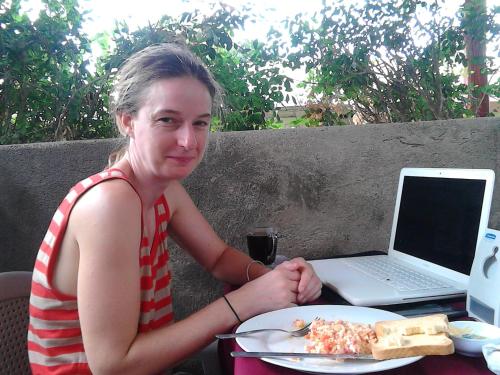 a woman sitting at a table with a plate of pizza and a laptop at Hostel Julieta in Rivas