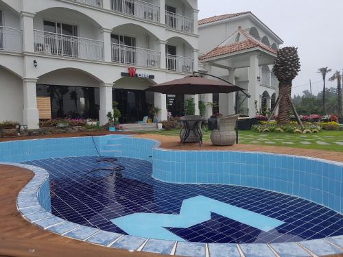 a pool in front of a building with an umbrella at MJ Pension & Resort in Seogwipo