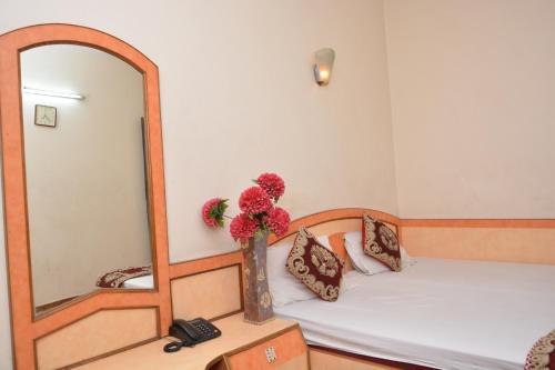 a room with a bed with a mirror and a vase with flowers at Hotel Yatri International in New Delhi
