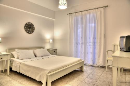 a white bedroom with a bed and a tv at Tzane Apartments in Chrissi Akti
