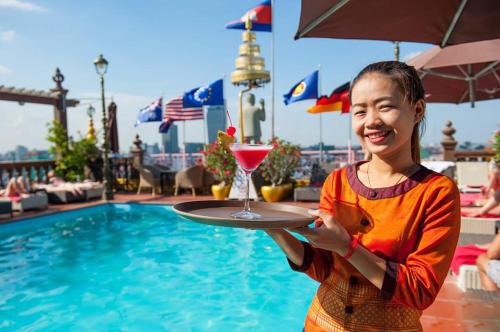 a girl holding a drink on a tray next to a pool at Okay Boutique Hotel in Phnom Penh