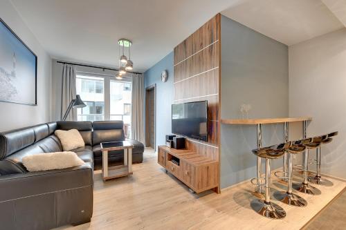 a living room with a black leather couch and a television at INA Rent - Tre Mare Apartamenty in Gdańsk