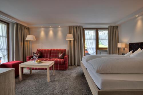 Hotel Gemma- Adults only في هيرشيغ: غرفة فندق بسرير واريكة حمراء