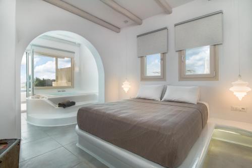 a bedroom with a bed and a bath tub and windows at Iphimedeia Luxury Hotel & Suites in Naxos Chora