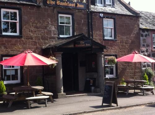 two tables and umbrellas in front of a building at Bankfoot Inn in Bankfoot