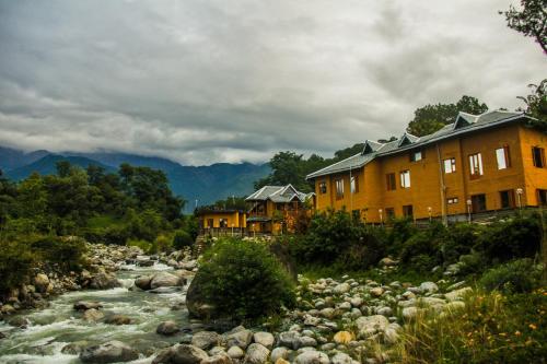 a river with houses next to a river with rocks at Prakriti Aalay - Riverside Mountain View Boutique Eco Resort in Dharamshala