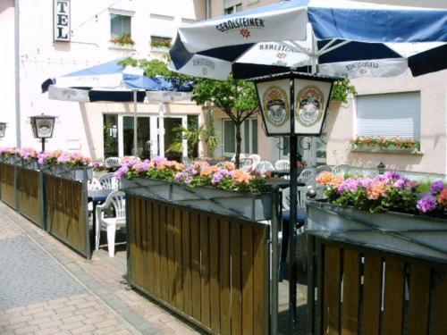 ein Café im Freien mit Blumen und einem Sonnenschirm in der Unterkunft Hotel zur Eisenbahn in Rodgau