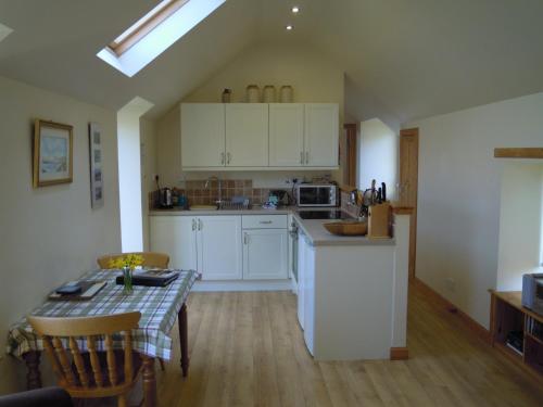 cocina con armarios blancos, mesa y comedor en The Smithy House & Cottages en Lochinver