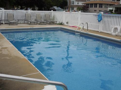 a large blue swimming pool with chairs and a fence at Pelican Point Motel in Point Pleasant Beach