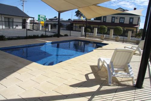 two chairs and an umbrella next to a swimming pool at Red Earth Motel in Broken Hill