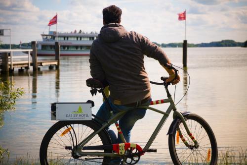 a man riding a bike next to a body of water at Das 53°Hotel in Bad Zwischenahn