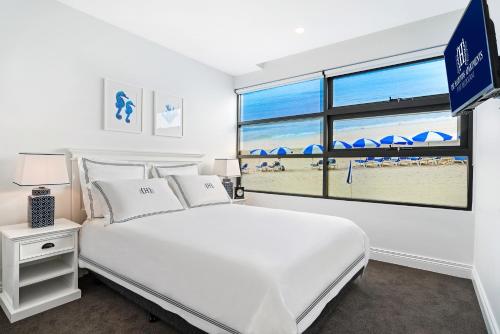 a bedroom with a bed and a window with a beach at The Hamptons Apartments - Port Melbourne in Melbourne