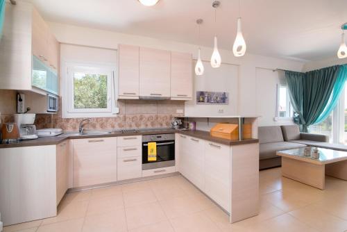 a kitchen with white cabinets and a couch at Olive Garden Villas and Apartments in Chrysi Ammoudia