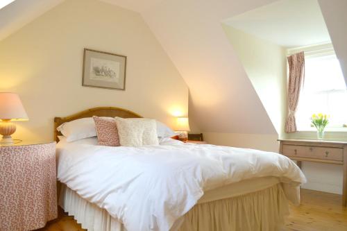 una camera da letto con letto, lenzuola e cuscini bianchi di Shelduck Cottage a Feorlean