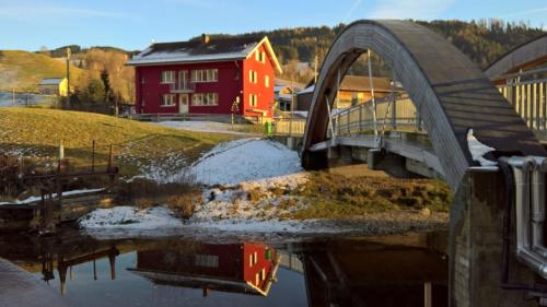 a bridge over a body of water with a red building at BnB chezlise in Urnäsch