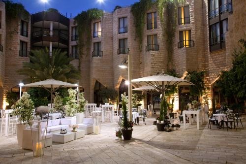 a courtyard with tables and umbrellas in front of a building at The Inbal Jerusalem in Jerusalem