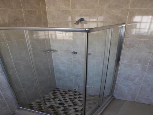 a shower with a glass door and a tiled floor at Divine Guest Lodge in Rustenburg