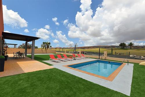 a swimming pool with chairs and a table and a patio at Villa Magna in Caleta De Fuste