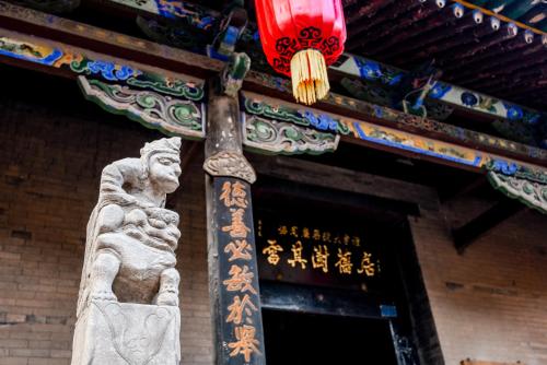 a statue in front of a building with a red lantern at Elsewhere Hotel The former residence of the draft bank in Pingyao