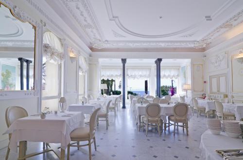 uma sala de jantar com mesas e cadeiras brancas em Hotel De Paris Sanremo em Sanremo