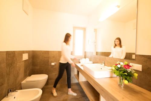 une femme debout dans une salle de bains avec lavabo dans l'établissement Panorama Hotel Flora, à Villandro