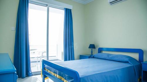 a bedroom with a blue bed and a large window at Paphinia SeaView Apartments in Paphos City