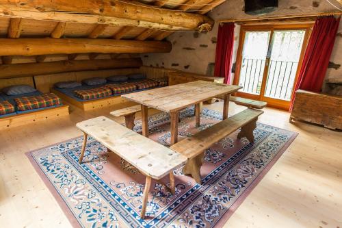 a wooden table and bench in a room with a rug at Rifugio Alpe San Romerio in Brusio