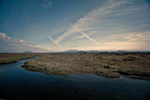 a river in the middle of a field with mountains at Borgarbæli in Hella