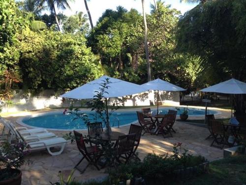 a patio with tables and chairs and umbrellas next to a pool at Pousada Araçás Village in Imbassai