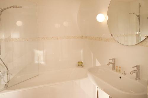 a white bathroom with a tub and a sink at Hôtel Parc Saint-Séverin - Esprit de France in Paris