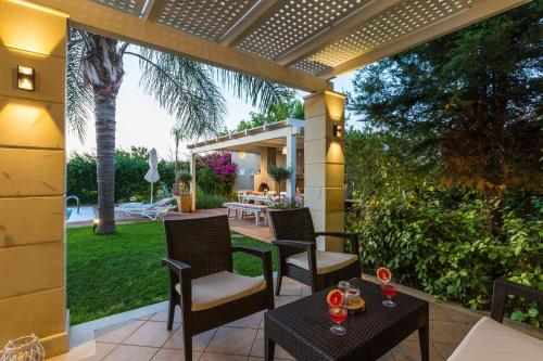 a patio with chairs and tables and a pergola at Aria Villas - Private Pool, Playground, Ping Pong & Close to Beach, By ThinkVilla in Pigi