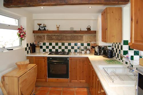 a kitchen with wooden cabinets and a stove top oven at May Cottage in Tideswell