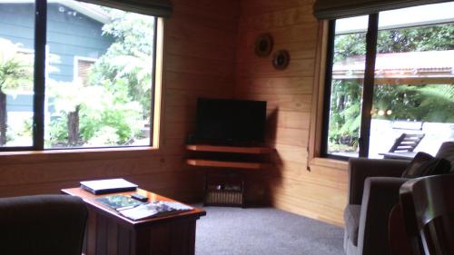 uma sala de estar com uma televisão, uma mesa e duas janelas em Creel Lodge em Turangi