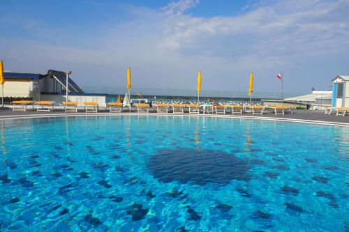 a large swimming pool with blue water and chairs at Hotel David in Cesenatico