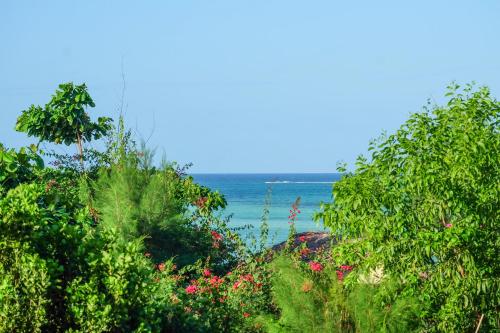 a view of the ocean through trees and flowers at Seasons Lodge Zanzibar in Pongwe