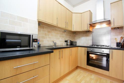 a kitchen with wooden cabinets and a microwave and a oven at Townhead Apartments Glasgow Airport in Paisley