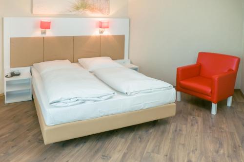 a bed and a red chair in a room at Hotel Stuttgart Sindelfingen City by Tulip Inn in Sindelfingen