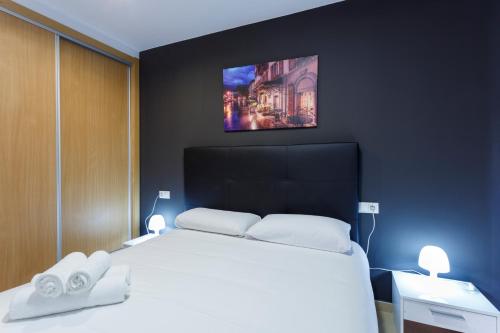 Schlafzimmer mit einem weißen Bett und einem TV an der Wand in der Unterkunft Apartamentos Santa Barbara in Alicante