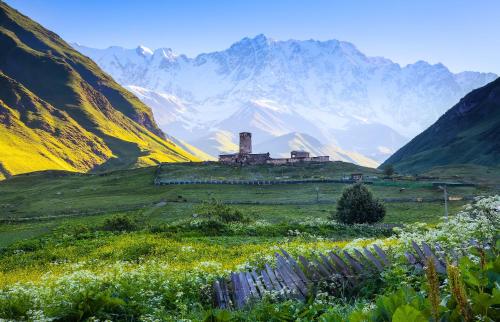 a painting of a house on a hill with mountains in the background at Guesthouse Angelina in Ushguli