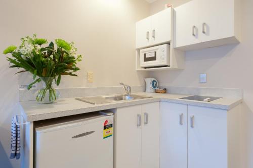 a kitchen with white cabinets and a vase of flowers at Outrigger Motel in Paihia